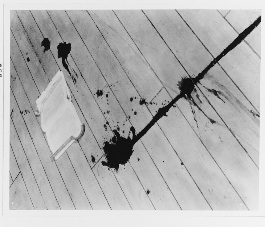 Trail of blood on the deck of USS Augusta from Seaman First Class Freddie J. Falgout, killed by splinters from an antiaircraft shell on 20 August 1937. The magazine that Falgout was reading while waiting for the movies to begin lies on the deck (NH 77831).