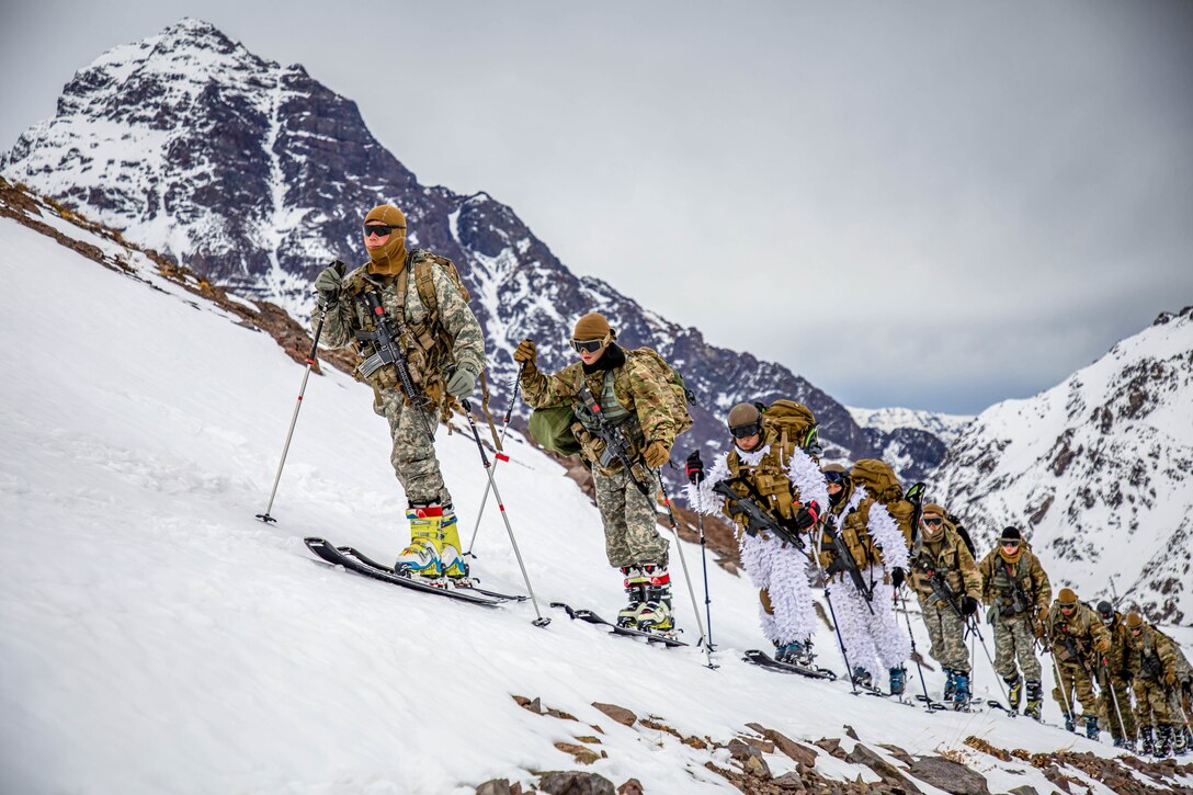A line of soldiers ski up the slope of a mountain.