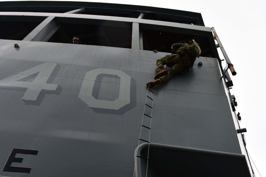 A U.S. Naval Special Warfare operator climbs aboard the Emory S. Land-class submarine tender USS Frank Cable (AS-40) during a boarding exercise as part of MALABAR 2021.