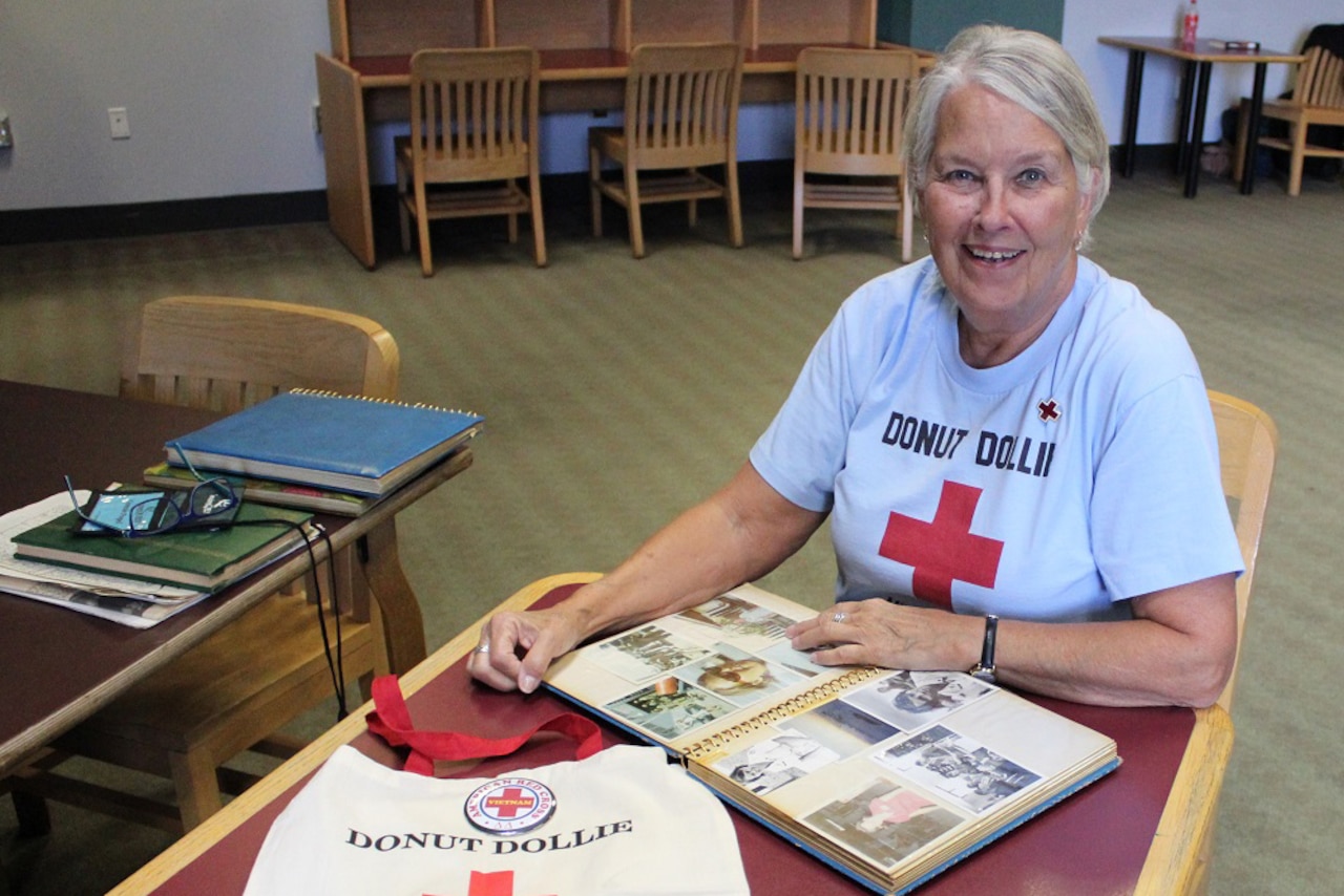 woman smiles while sitting at a table with an open scrapbook.