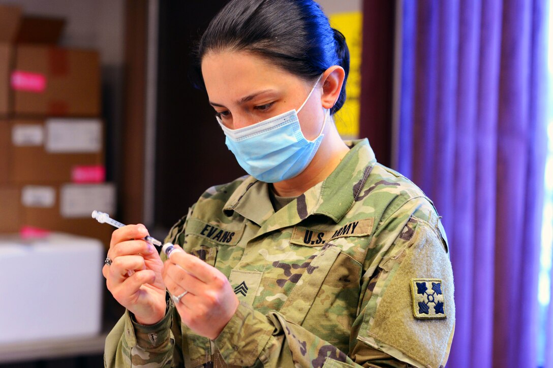 A soldier wearing a face mask holds a syringe.