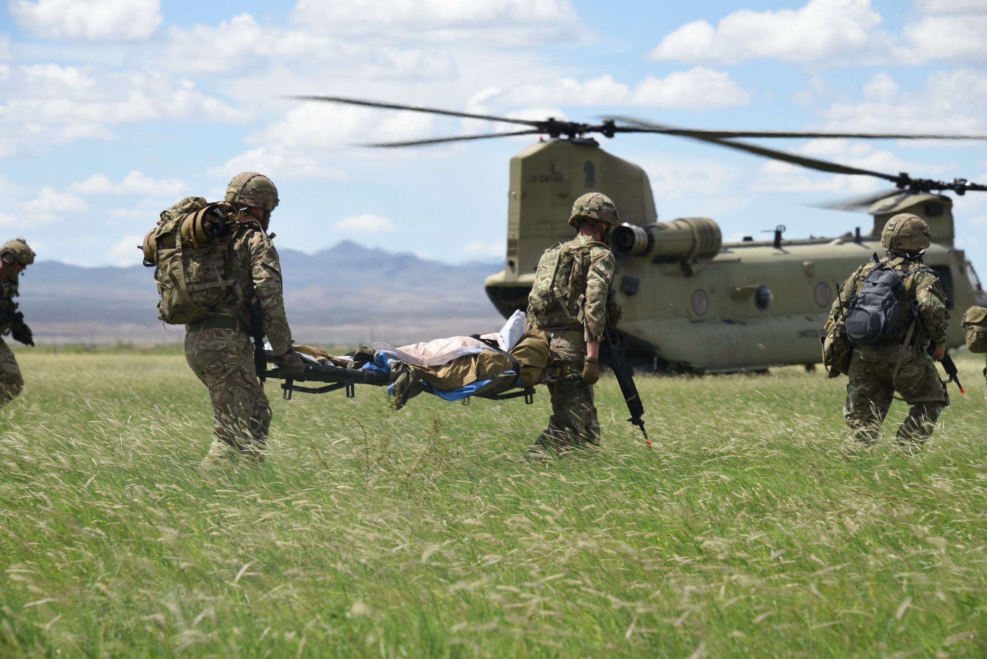 A photo of pararescuemen carrying a simulated casualty towards a chinook helicopter.