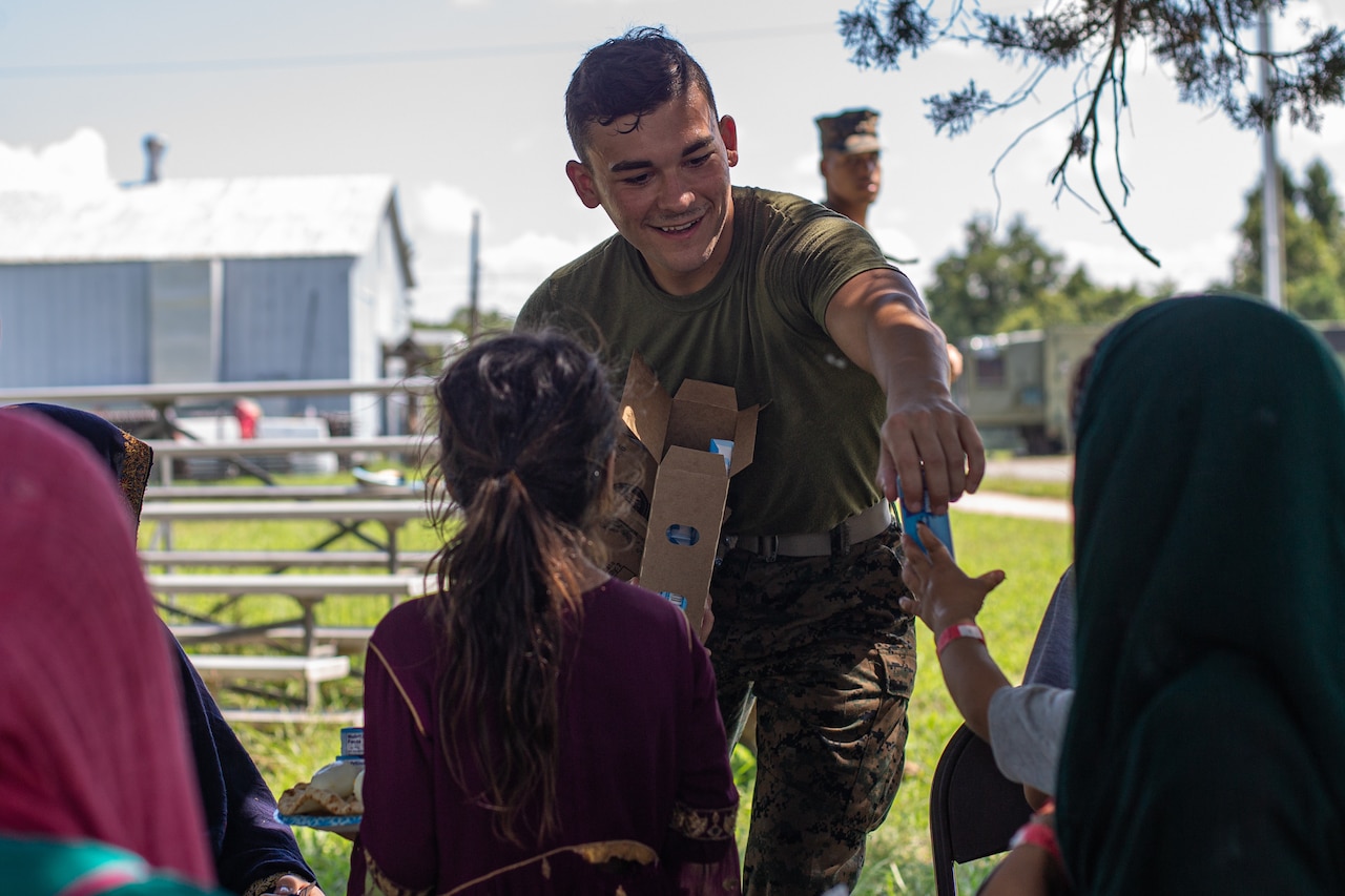 A service member hands ice cream to young children.
