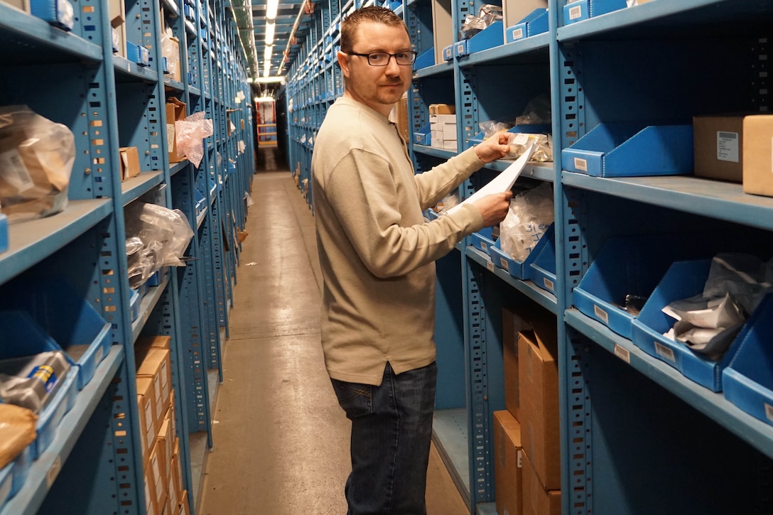 A man stands next to shelves in a warehouse.
