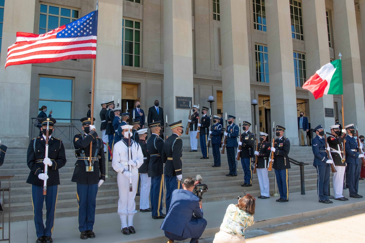 Two men stand on steps flanked by service members.