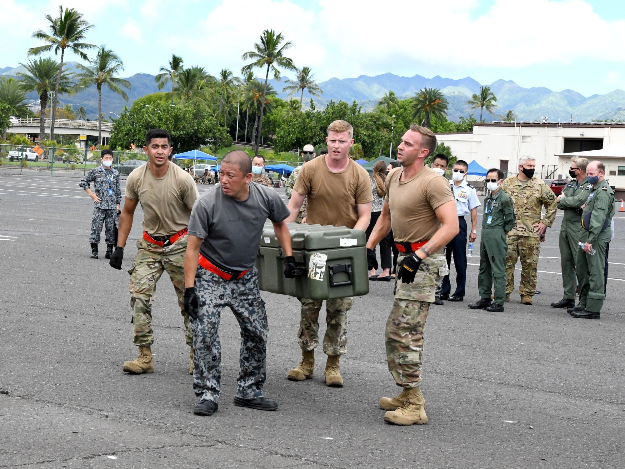 Four Airmen carry a large box as a crowd watches.