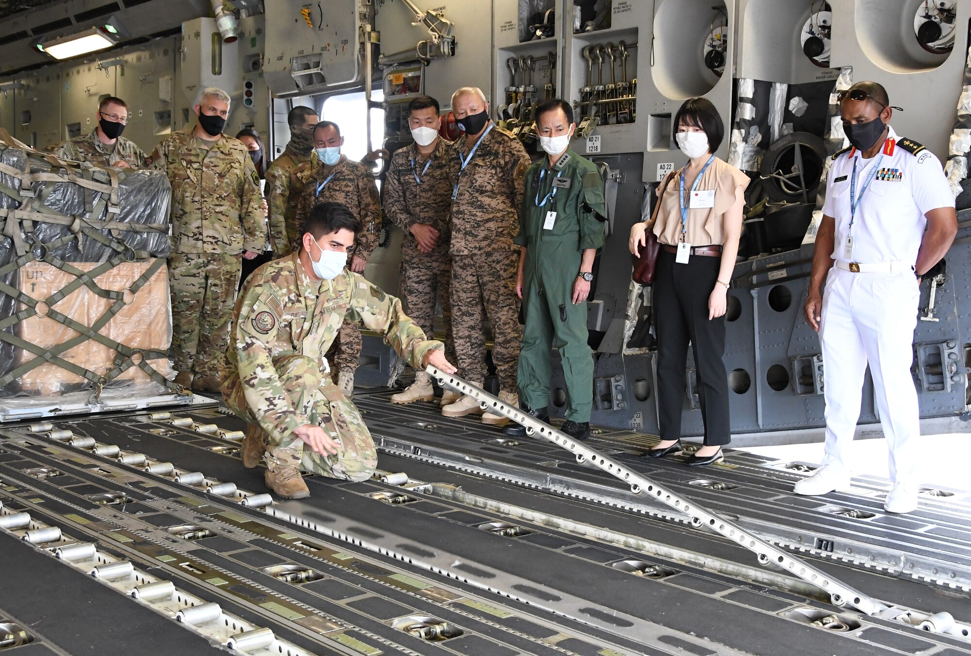 SSgt. Andrew Flint lifts up a track inside of a C-17 Globemaster as a group of international partners watches.