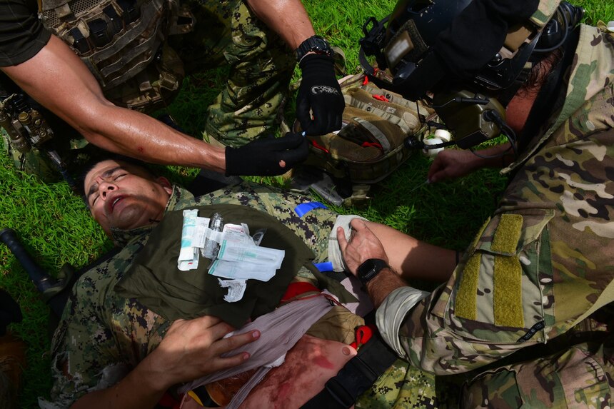 U.S. Naval Special Warfare (NSW) operators start an IV for a simulated wounded service member during an urban combat training scenario as part of MALABAR 2021.