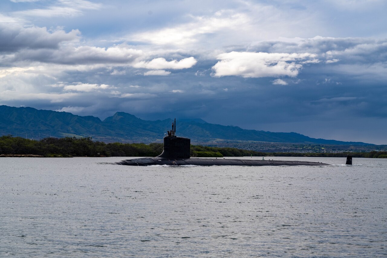 A submarine steams out of a harbor.