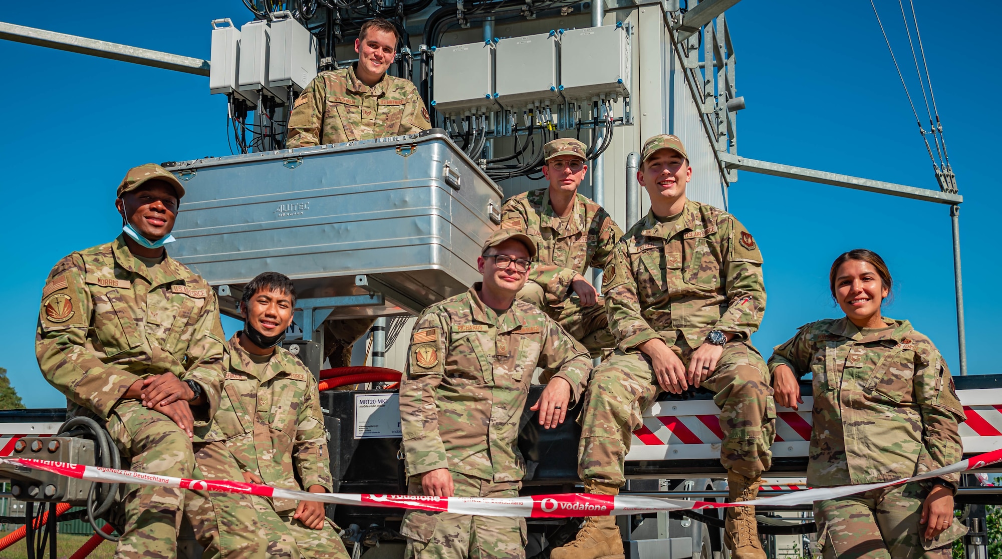 Airmen pose for photo in front of mobile 5G tower.