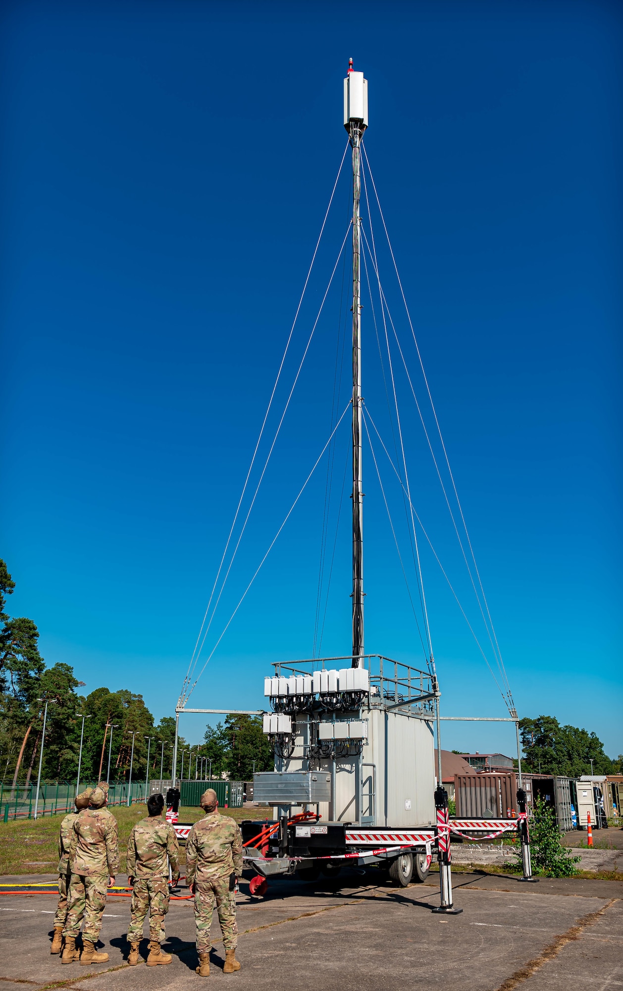 Airmen stand next to mobile cell tower.