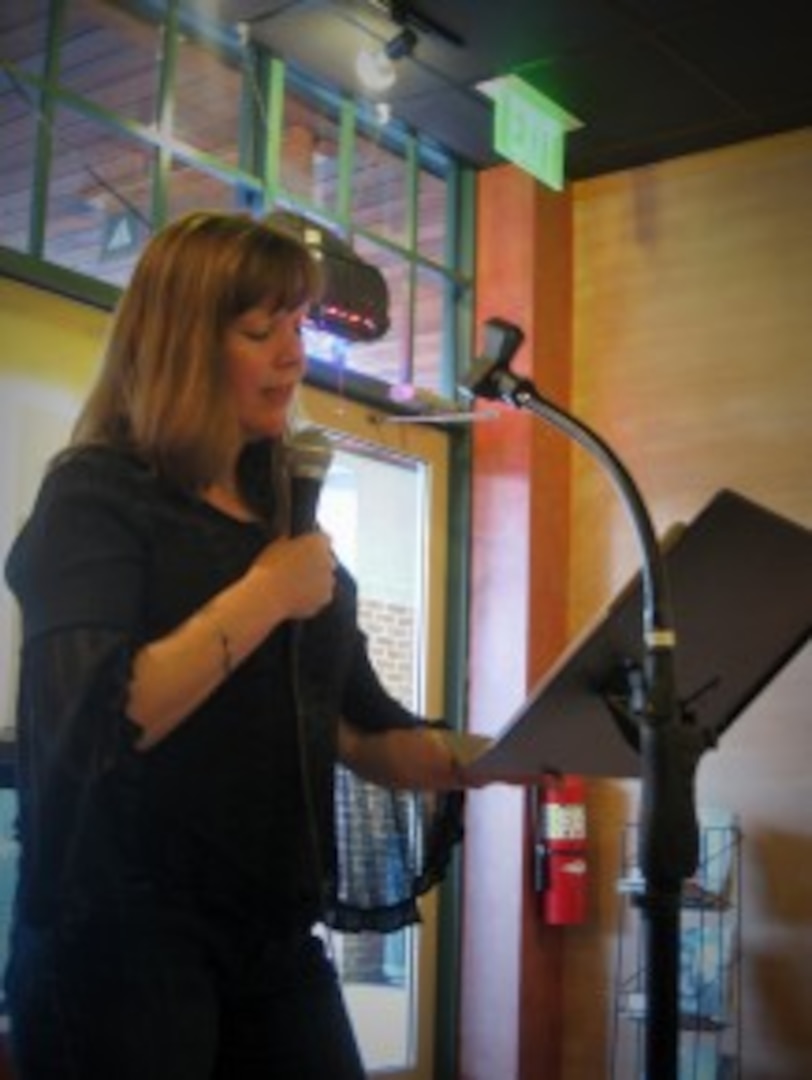 Diane Guarnieri, published poet and Defense Logistics Agency Troop Support employee, performs a poem aloud with a microphone while standing at a podium.