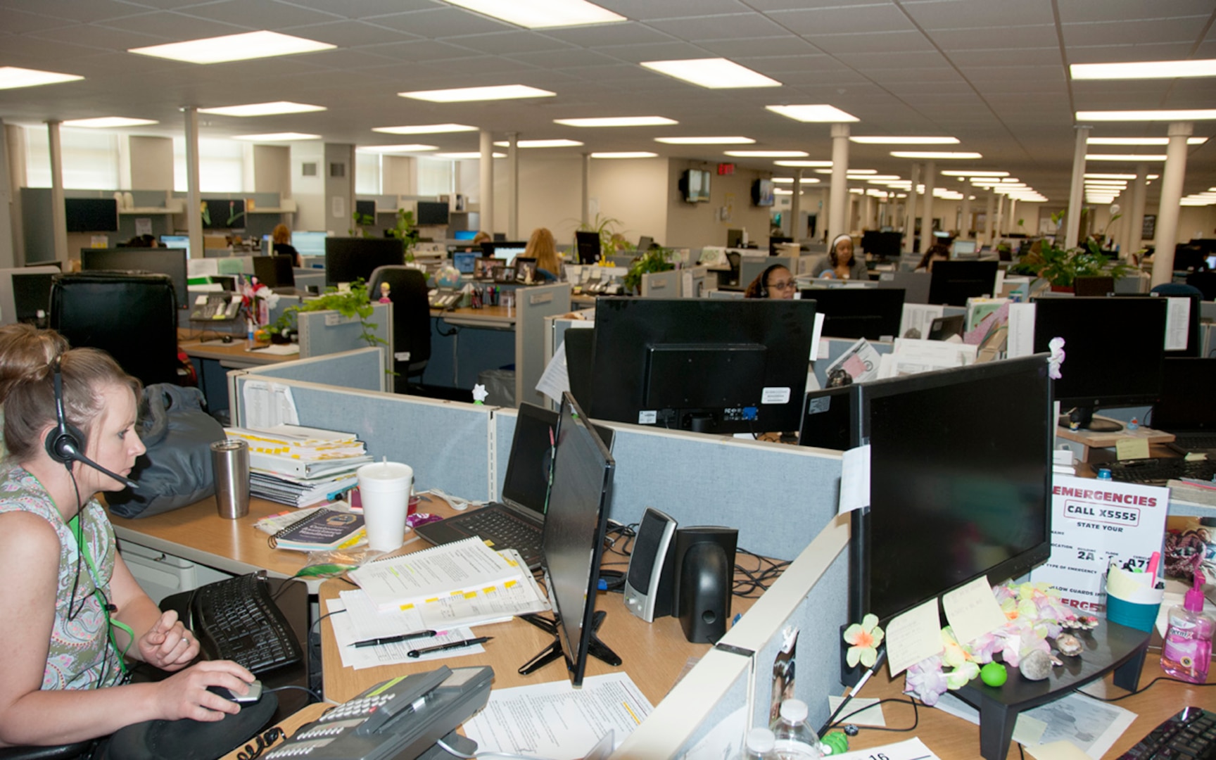 Workers sit in front of computers in an open bay office