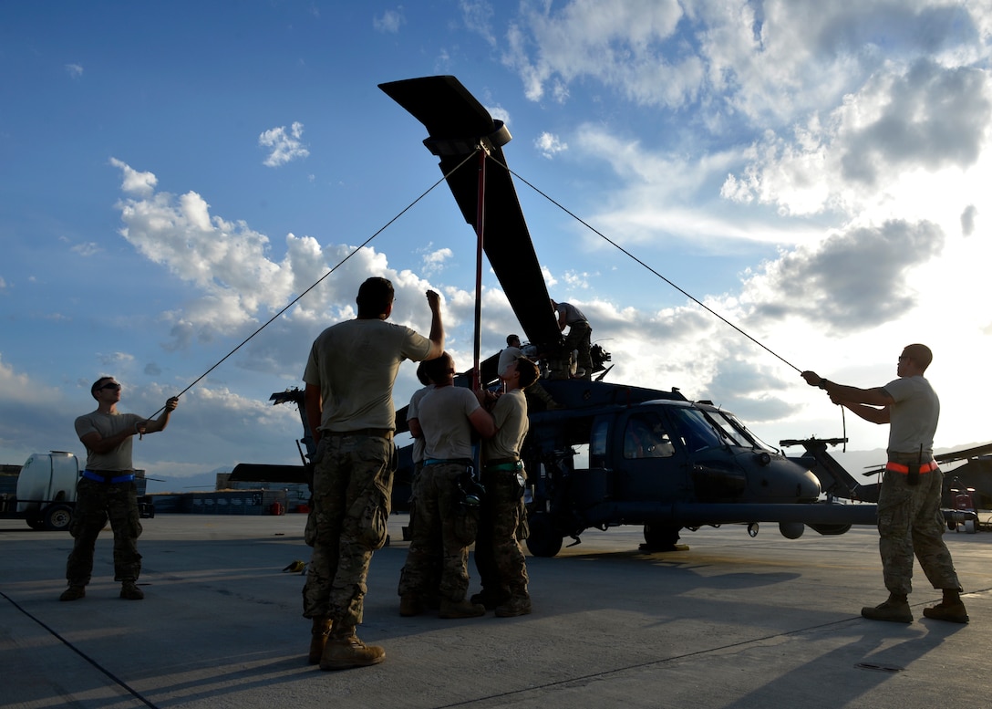 Soldiers stand around an airplane pulling ropes from the blades under a blue and white sky.