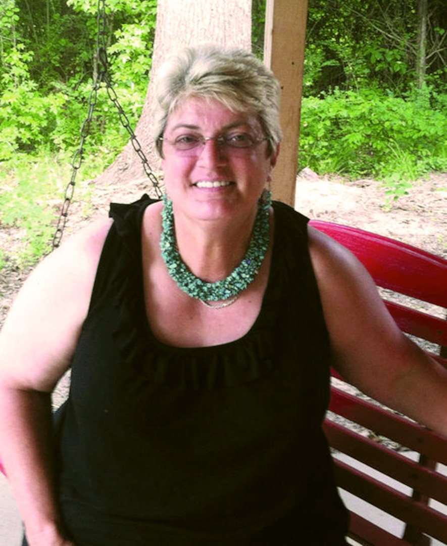 Woman wearing a black shirt and blue necklace sits on a red metal chair outside