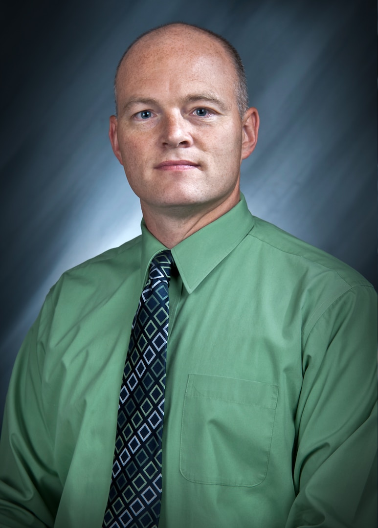 Head and shoulders portrait of a man wearing a green shirt and blue tie