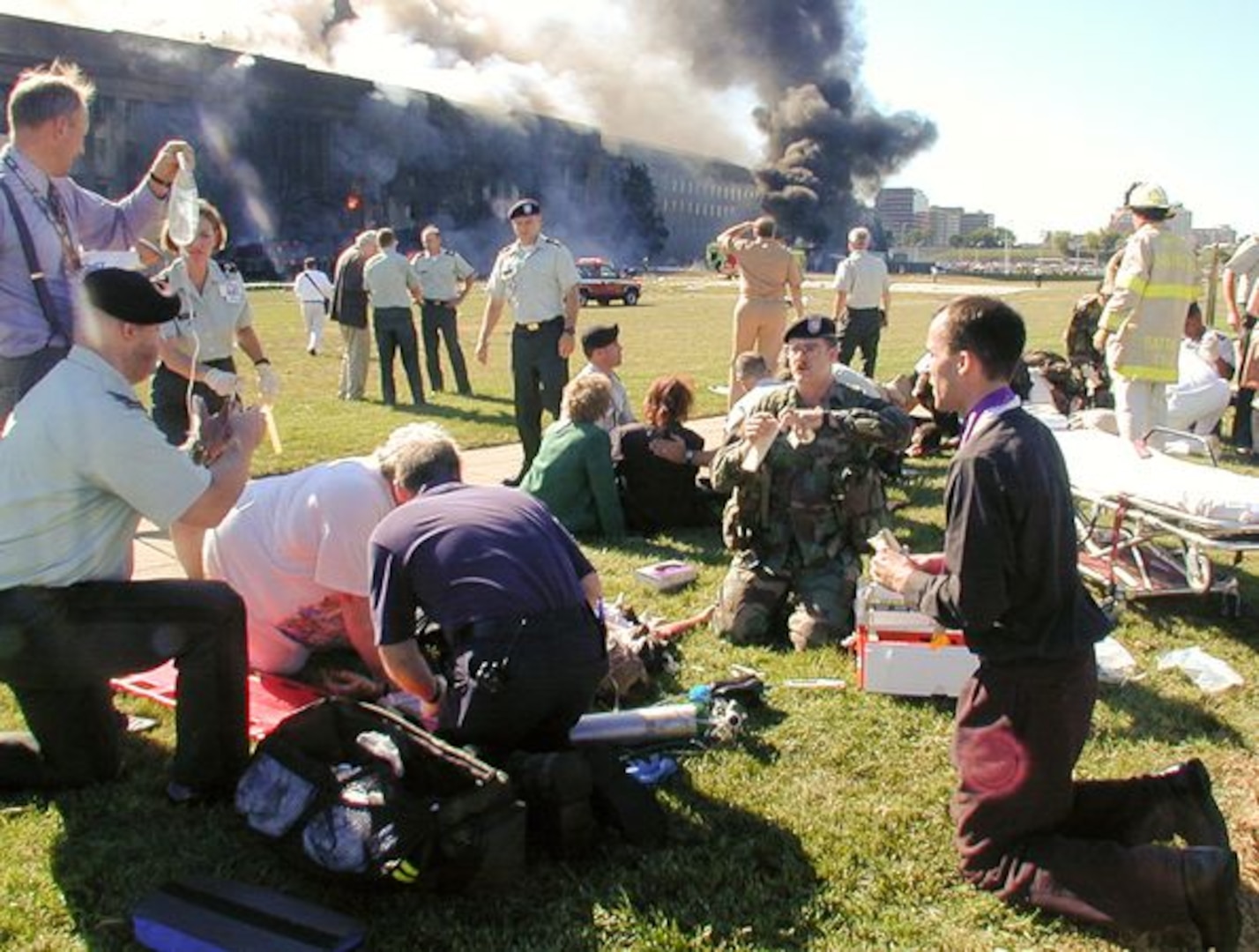 Men and women are scattered on the grass outside of a smoking building.