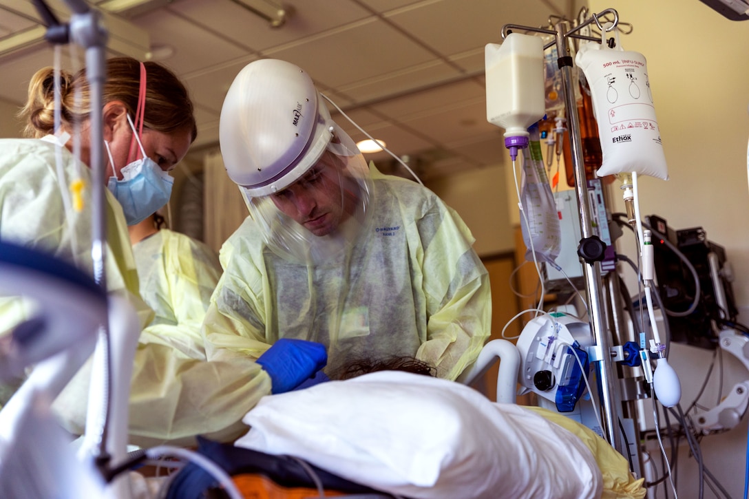 A woman wearing a face mask, gloves and medical gown and a man wearing personal protective equipment work with a patient.