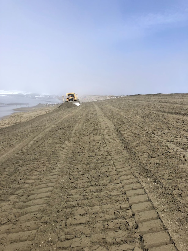 Sloping sand down to water with a bulldozer off in the distance.