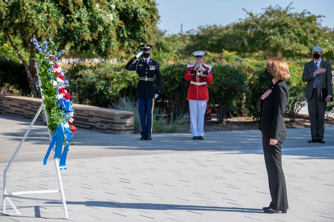 Deputy defense secretary holds hand over her heart while facing a wreath display.