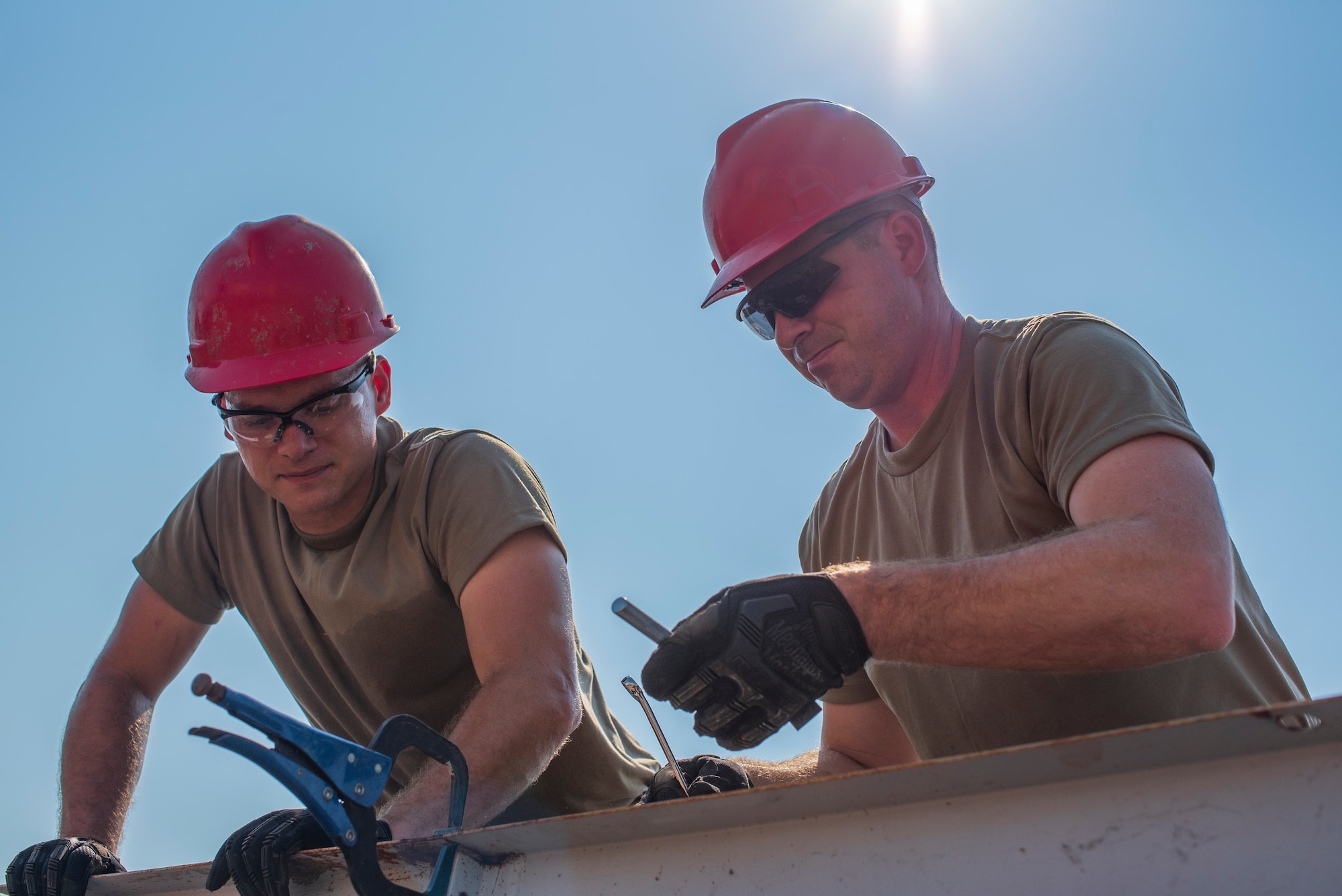 Two men work wearing red hard hats and the Air Force OCP uniform.