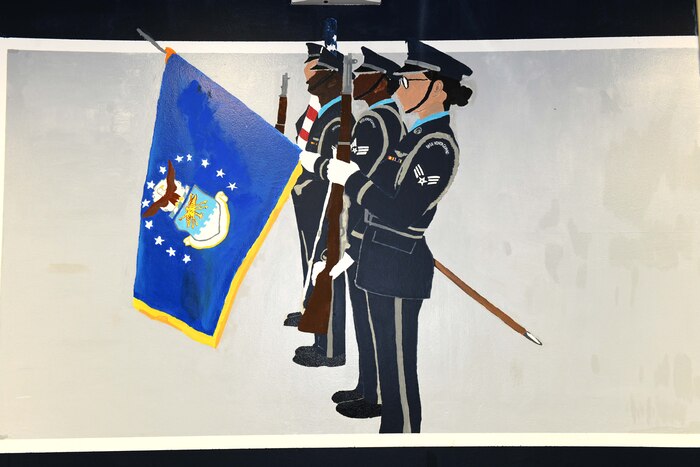 Photo shows a wall painting of four honor guard members carrying flags and rifles