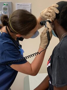 Lt. Francesca Reside, a medical officer assigned to U.S. Navy Medicine Readiness and Training Command (NMRTC) Naples, checks a student’s ear with her otoscope as part of a school physical clinic aboard Naval Support Activity Naples, Aug. 28, 2021. NMRTC Naples sponsored a clinic offering sports physicals, school entrance physicals, immunizations, and COVID-19 vaccines on base from Aug. 26-28.  (U.S. Navy photo by Hospital Corpsman 3rd Class Anthony Quinteros).