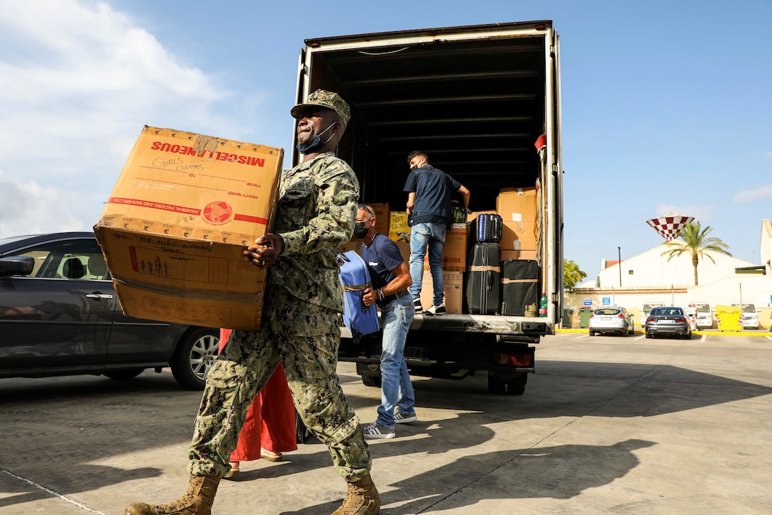 A sailor and volunteers unload boxes from a truck.
