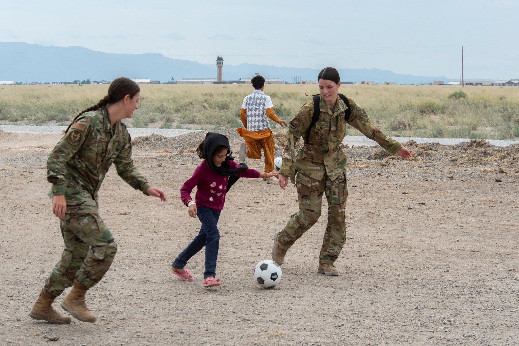 Airmen from Task Force-Holloman play soccer with an Afghan evacuee at the Afghan personnel camp on Holloman Air Force Base, New Mexico, Aug. 31, 2021. The Department of Defense, through U.S. Northern Command, and in support of the Department of State and Department of Homeland Security, is providing transportation, temporary housing, medical screening, and general support for up to 50,000 Afghan evacuees at suitable facilities, in permanent or temporary structures, as quickly as possible. This initiative provides Afghan evacuees essential support at secure locations outside Afghanistan. (U.S. Air Force photo by Staff Sgt. Kenneth Boyton)