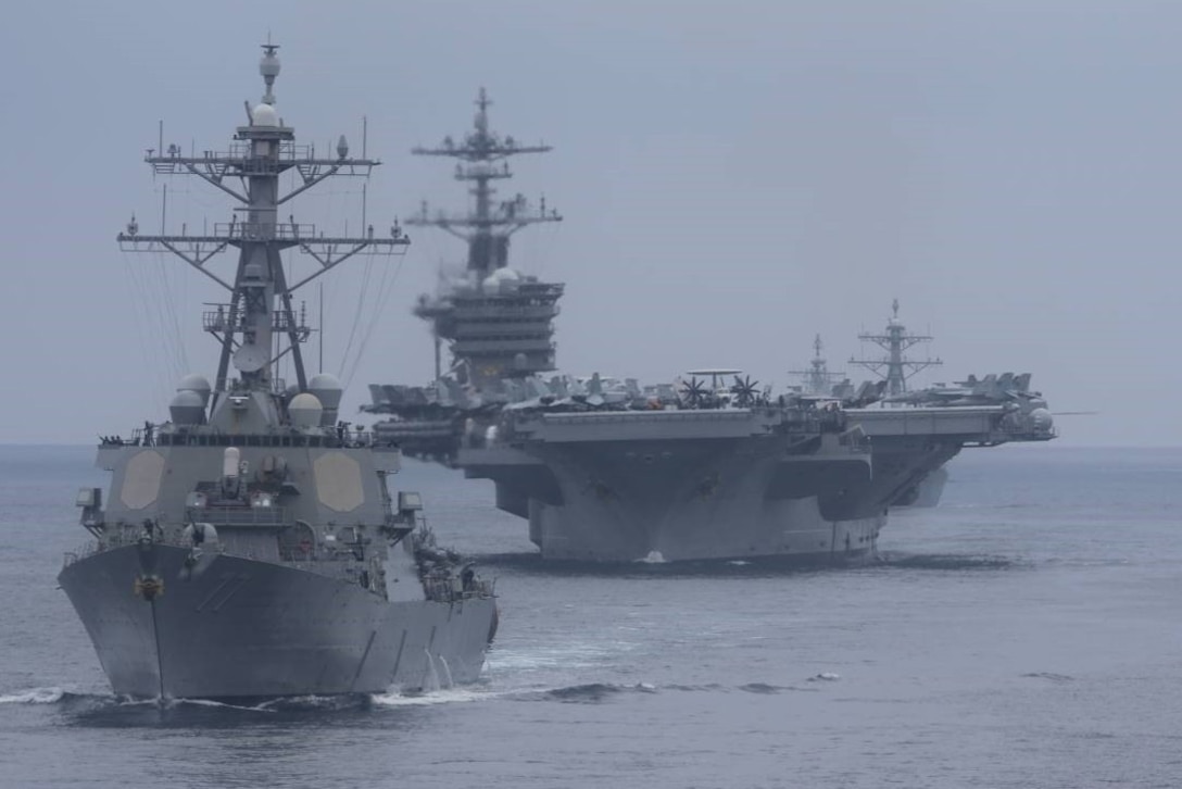 Large military ships move through the ocean.