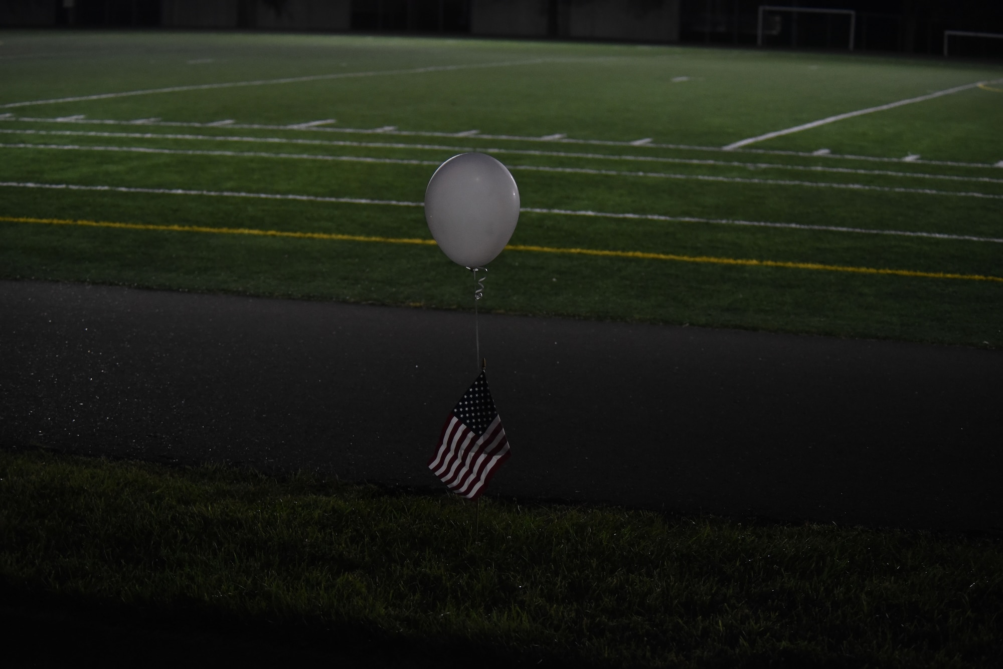 A balloon hangs onto a flag at a track at night.