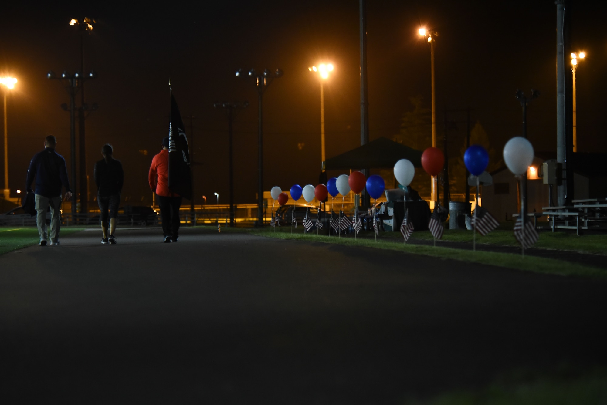 Members hold up the POW/MIA flag in a track at night.