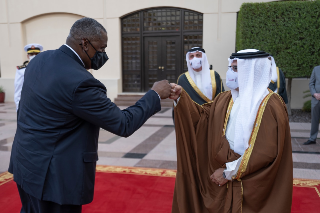 A man dressed in a business suit bumps fists with a man dressed in Middle Eastern attire.