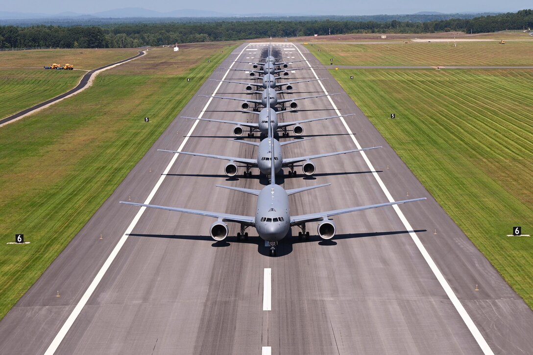Seven aircraft sit in a straight line on a tarmac.