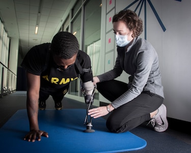 Occupational therapist assisting male soldier with prosthetic arm with pushups.