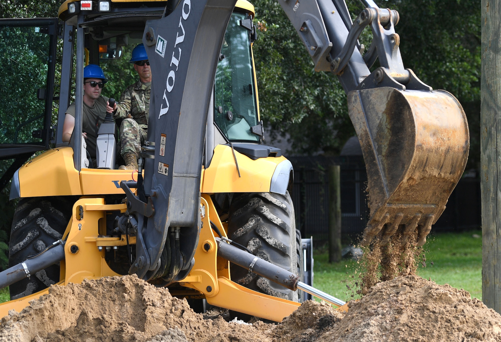 U.S. Air Force Col. William Hunter, 81st Training Wing commander, operates a backhoe with the assistance of Staff Sgt. Chase Kiefer, 85th Engineering Installation Squadron cable and antenna systems technician, during an 85th EIS immersion tour behind Maltby Hall at Keesler Air Force Base, Mississippi, Sept. 1, 2021. The purpose of the tour was to become more familiar with the squadron's mission and its capabilities. (U.S. Air Force photo by Kemberly Groue)