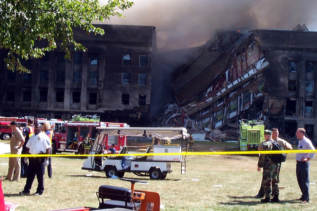 A collapsed building is shown. Smoke rises.