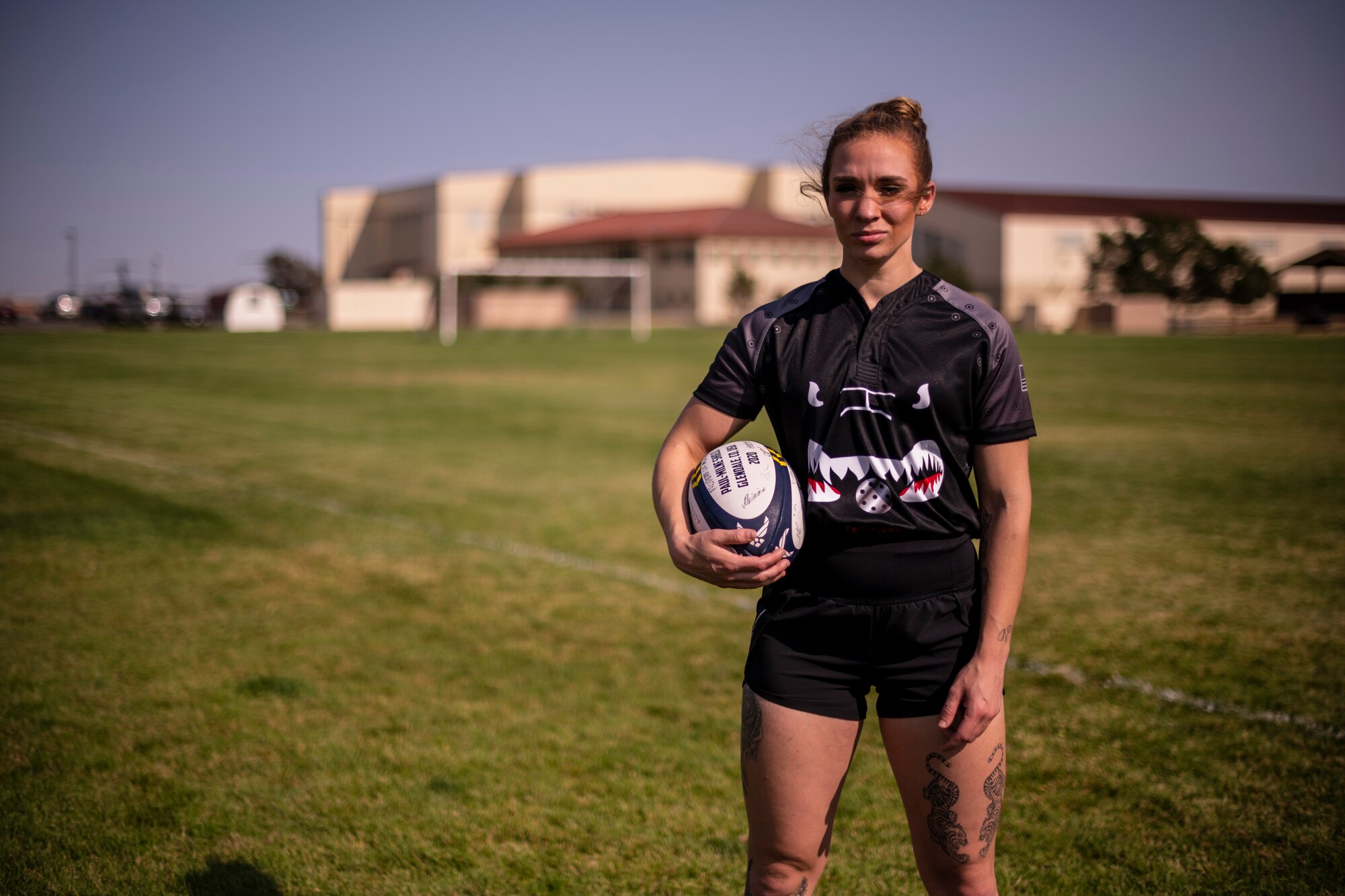 A woman stand on a soccer field holding a rugby ball.