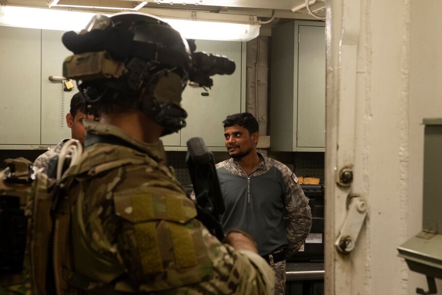 A naval special warfare operator talks with Indian navy sailors during a boarding drill aboard USNS Pililaau (T-AK 304)during MALABAR 2021.