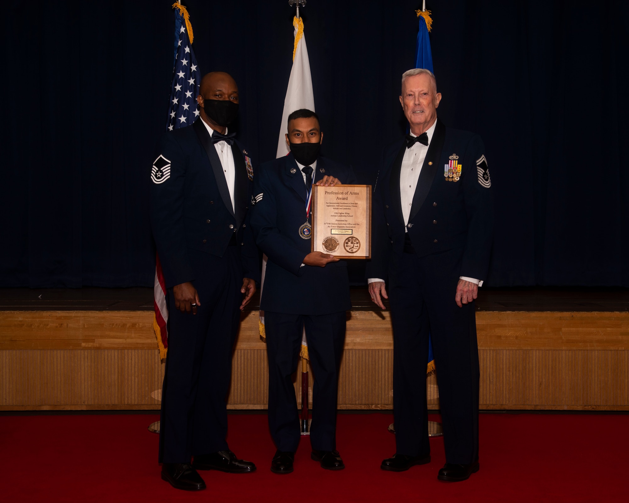 Military members in uniform pose with an award for a photo