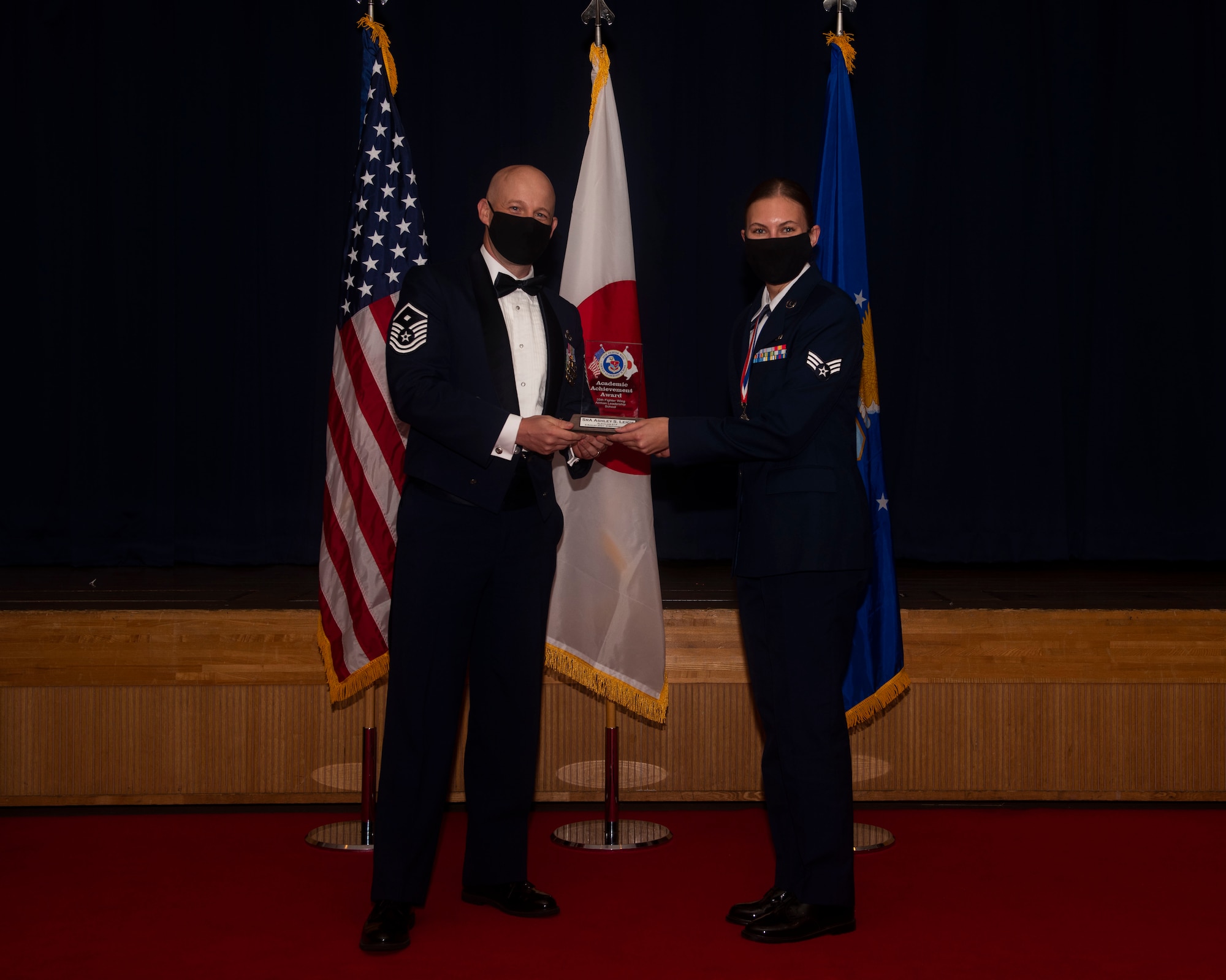 Military members in uniform pose with an award for a photo