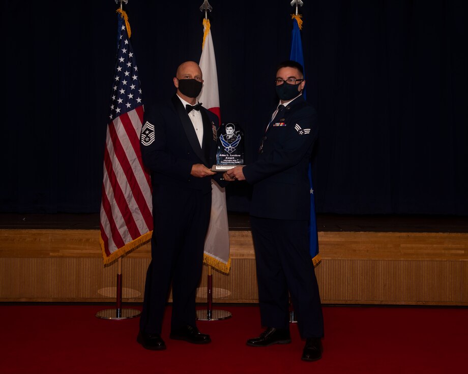 Military members in uniform pose with an award for a photo