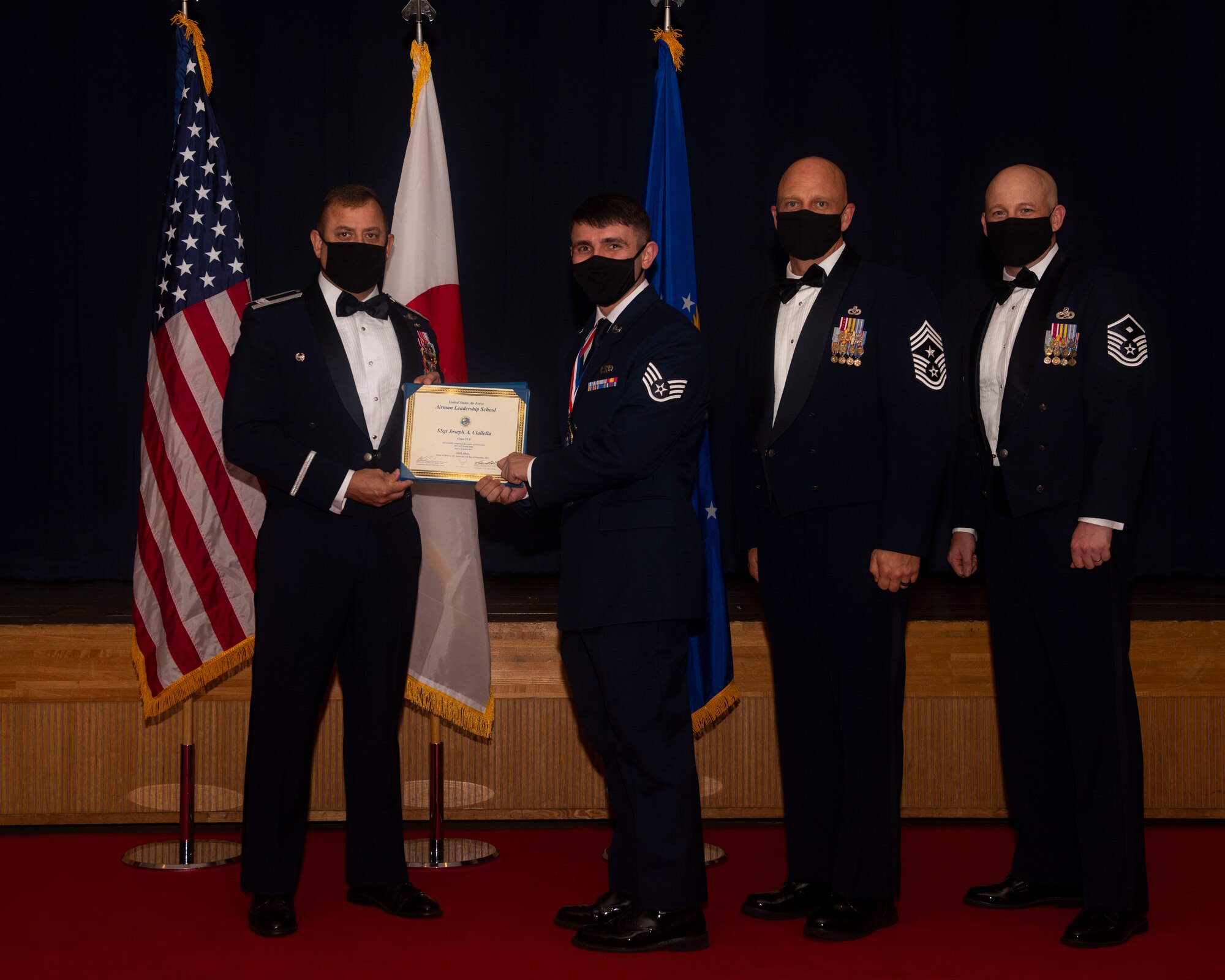 Military members in uniform pose with a diploma for a photo