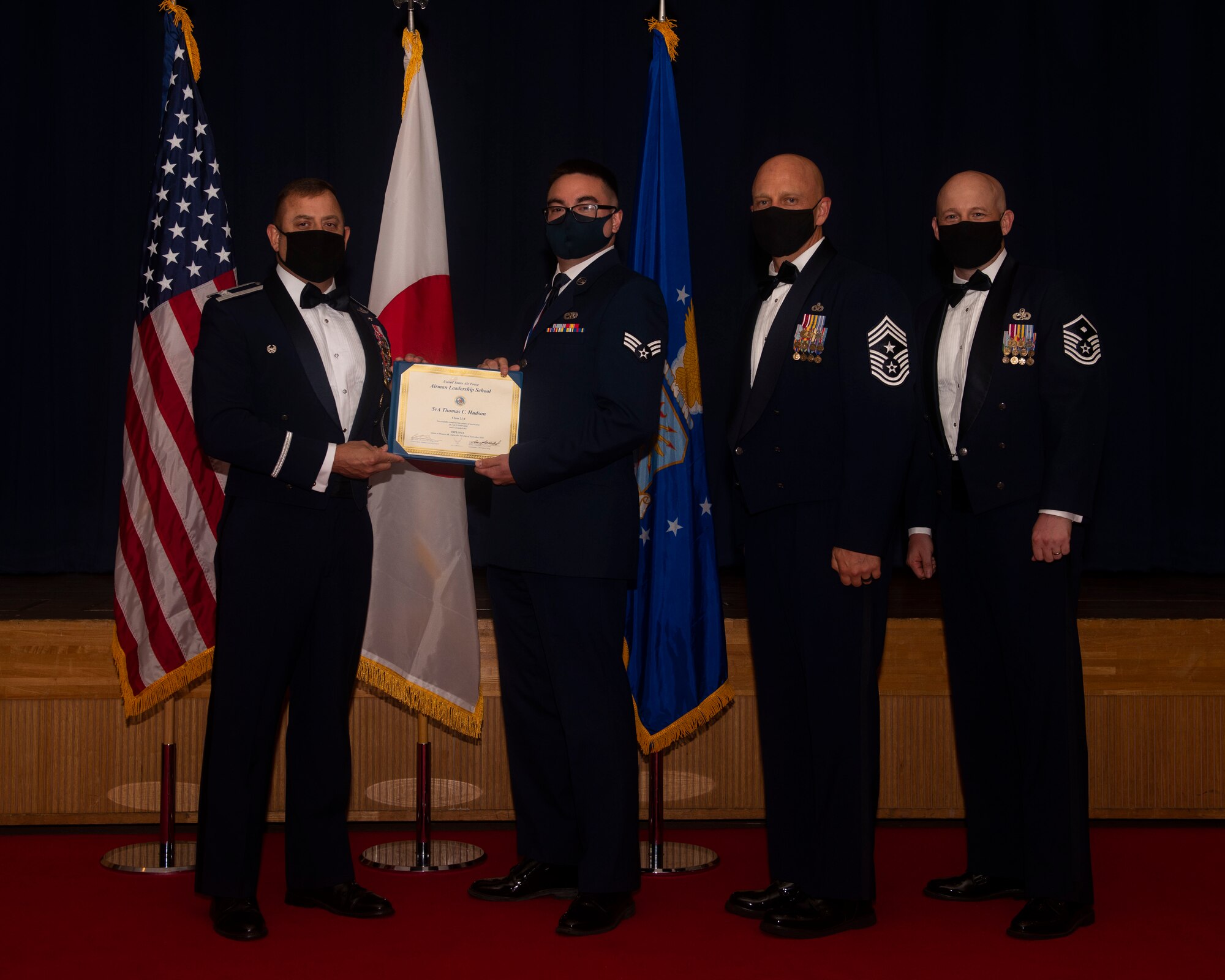 Military members in uniform pose with a diploma for a photo