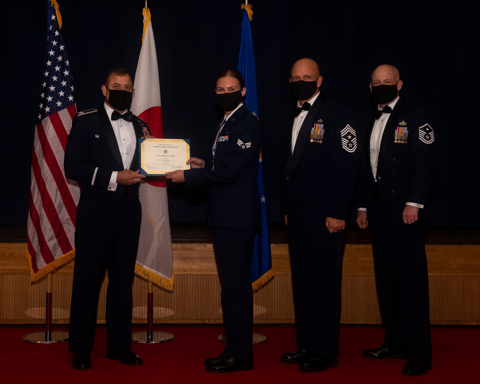 Military members in uniform pose with a diploma for a photo