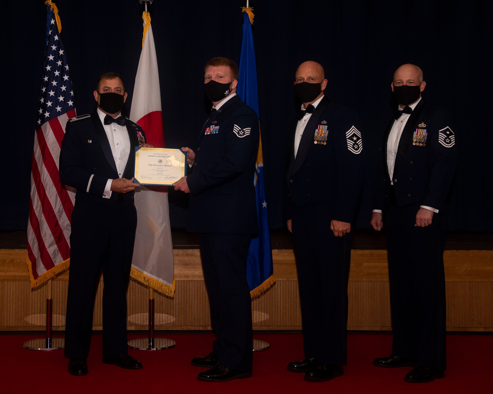 Military members in uniform pose with a diploma for a photo