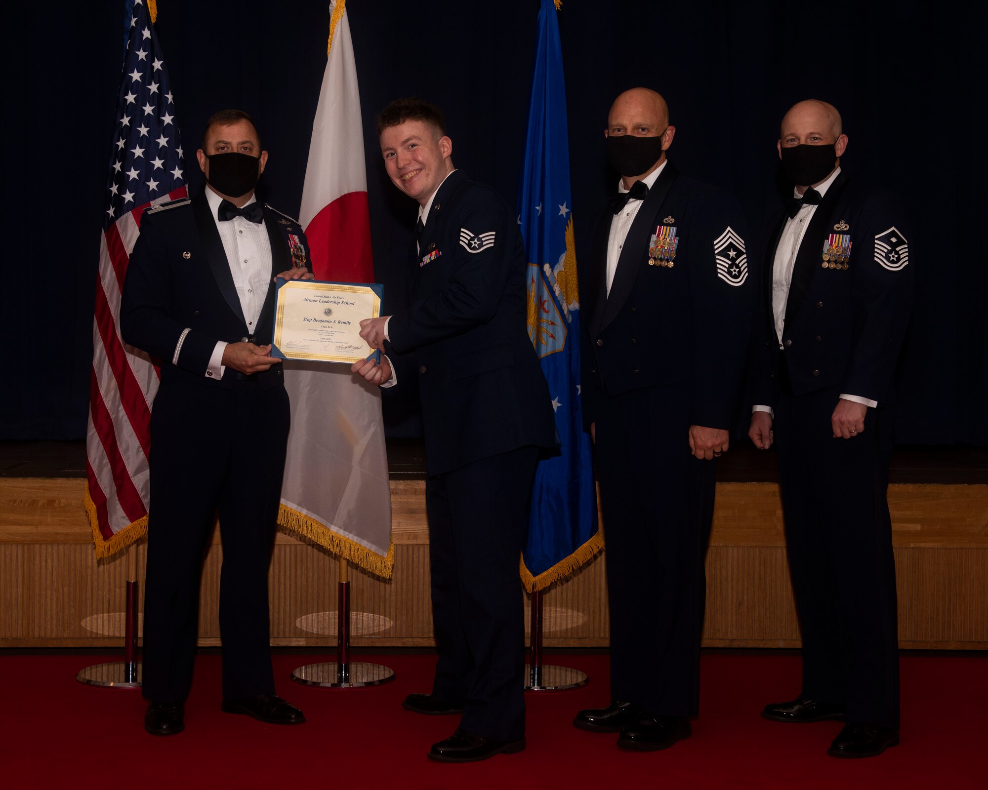 Military members in uniform pose with a diploma for a photo