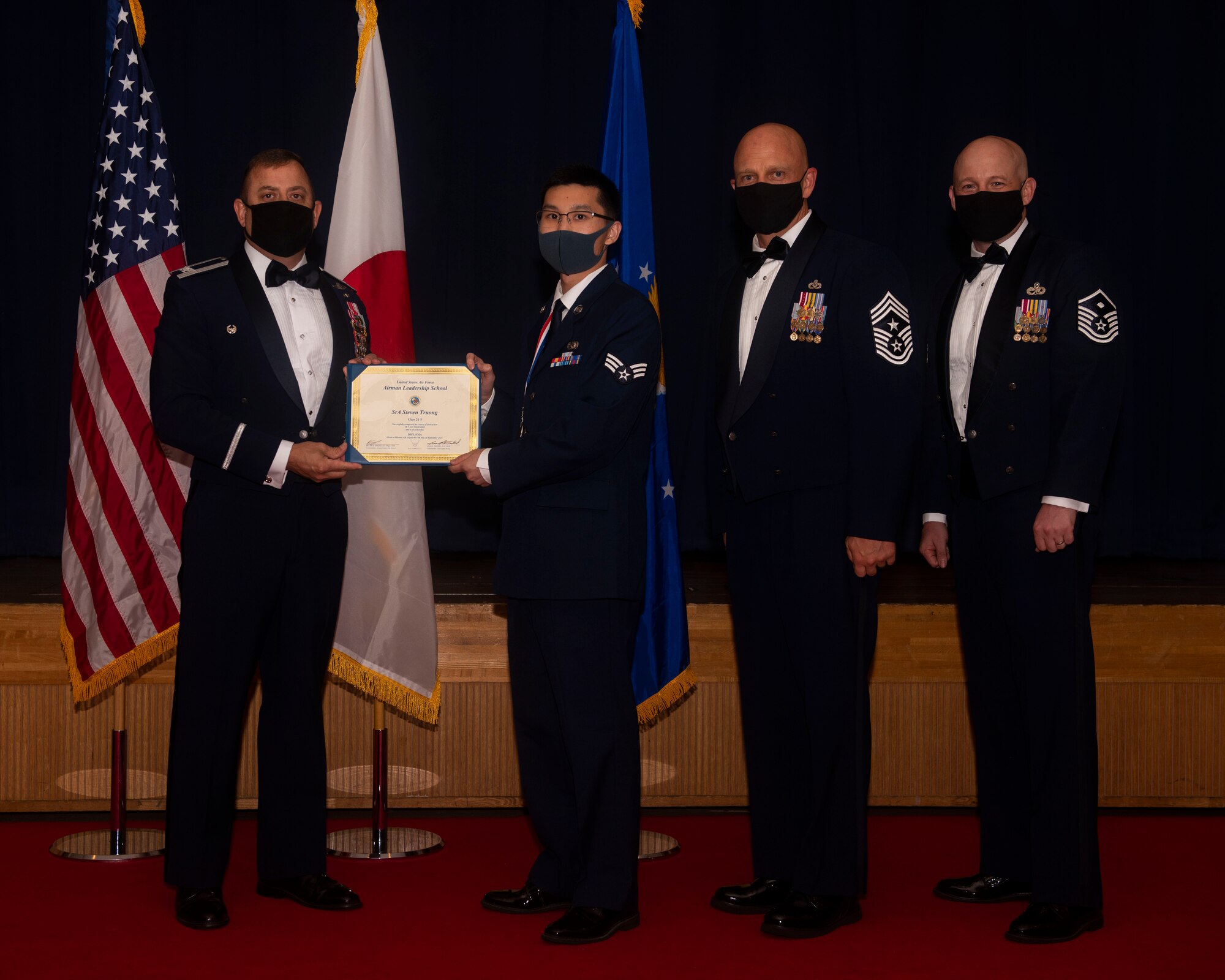 Military members in uniform pose with a diploma for a photo