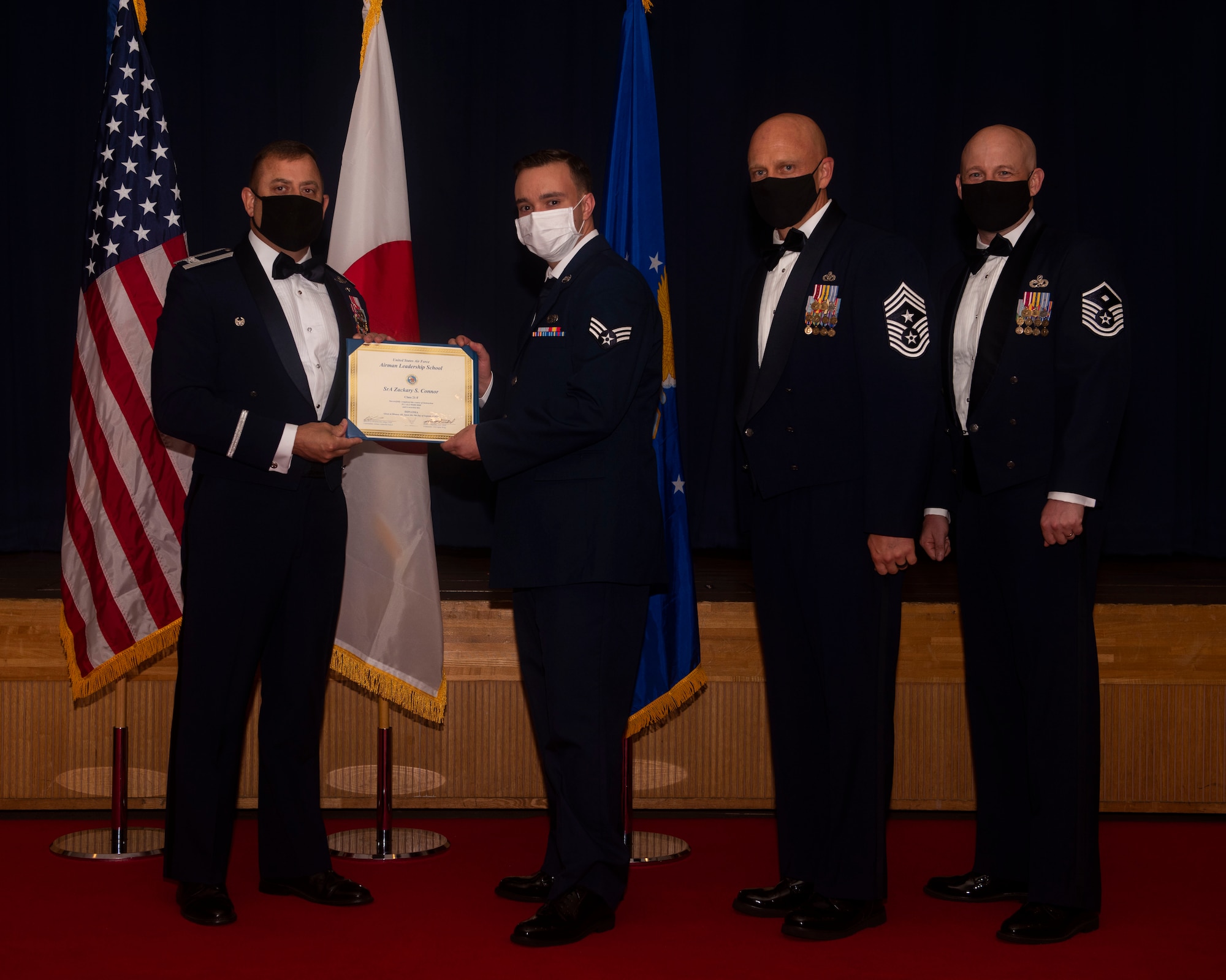Military members in uniform pose with a diploma for a photo