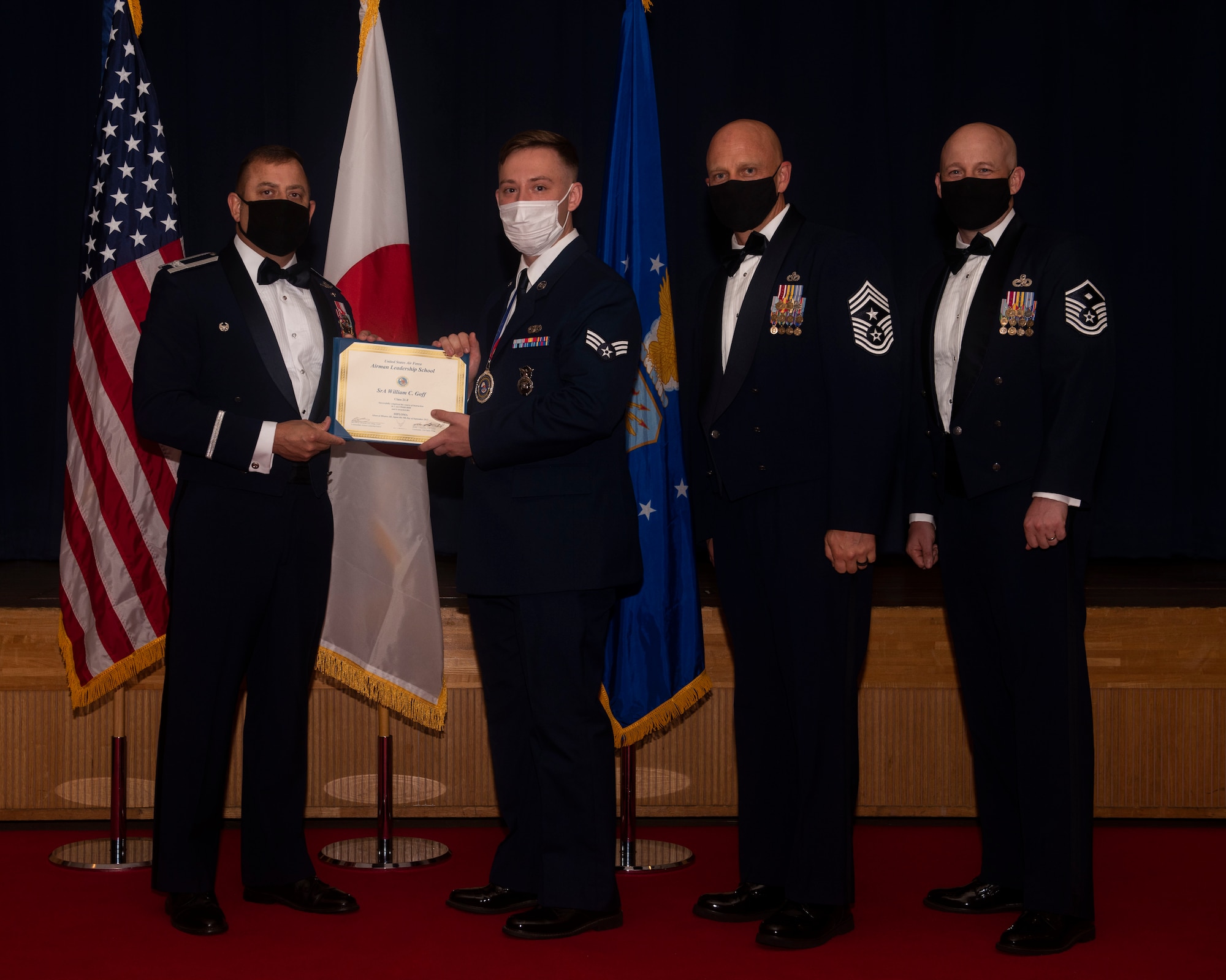 Military members in uniform pose with a diploma for a photo